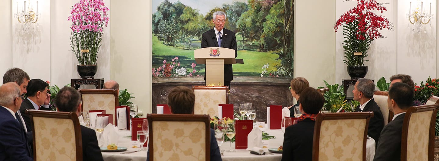 Lee Hsien Loong speaks at a podium with the Singapore coat of arms, viewed by seated diners.